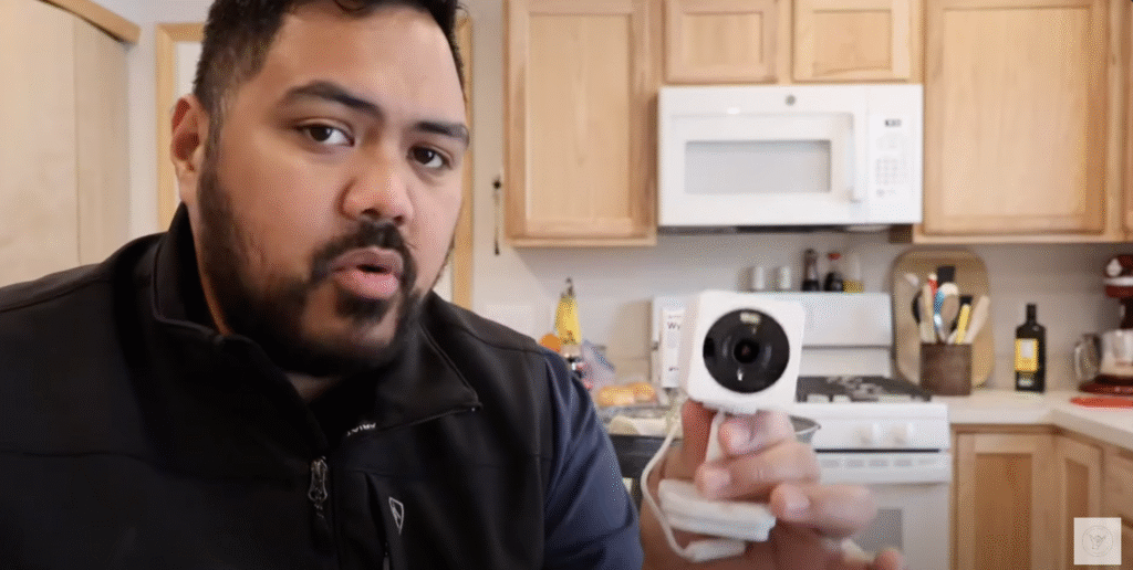 Content creator holding a white Wyze security camera in a kitchen setup, providing a hands-on review.